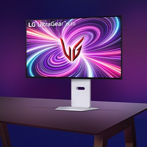 보라색 그라데이션 배경의 어두운 책상 위에 LG 울트라기어 모니터가 놓여 있습니다. 모니터 화면에는 분홍색과 보라색이 섞인 화려한 소용돌이 패턴 중앙에 빨간색 'UG' 로고가 배치되어 있으며, 화면 왼쪽 상단에는 'LG UltraGear OLED'라는 문구가 적혀 있습니다.