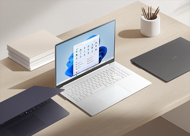 밝은 책상 위에 다양한 색상의 노트북 3대와 책, 연필꽂이가 정돈된 상태로 놓여 있다.